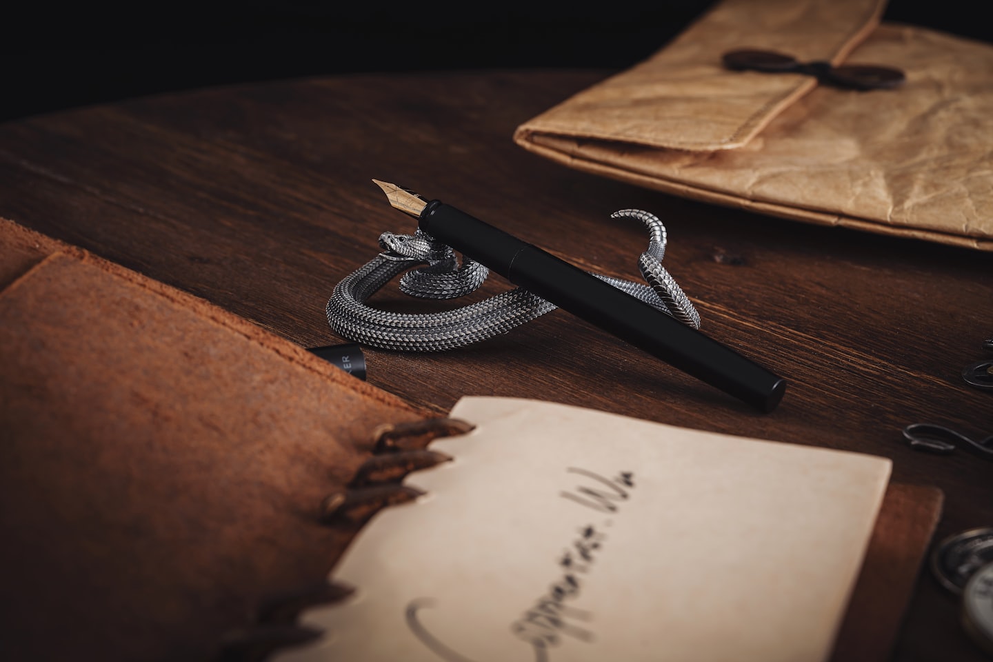 A black fountain pen rests on a silver holder beside an open journal.